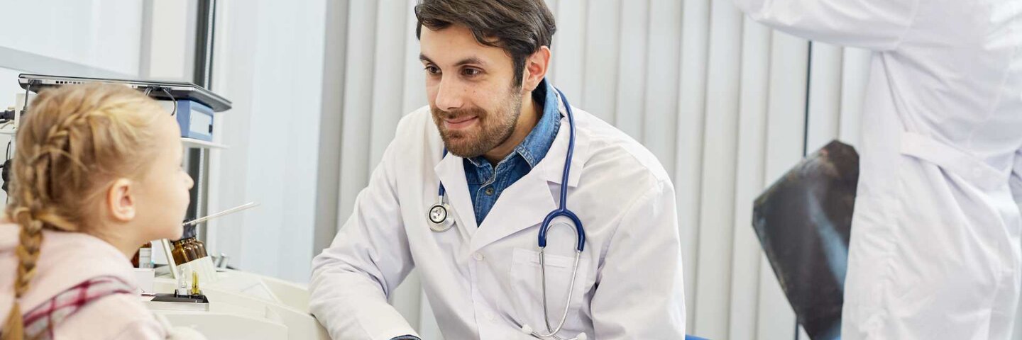 Male doctor talking with child patient while his colleague working in the background