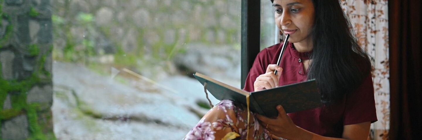 Woman writing in a diary sitting at the window