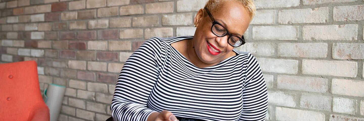  Older Black woman seated in a chair making an outline in her notebook.