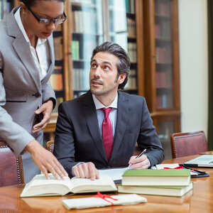 two business professionals in suits referring to an open law book